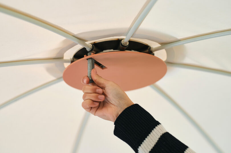 A hand adjusting a metallic rod on a canopy.